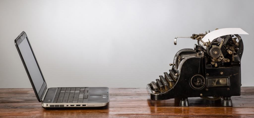 Vintage typewriter beside a modern laptop on a wooden desk, illustrating lessons from famous writers for content marketing