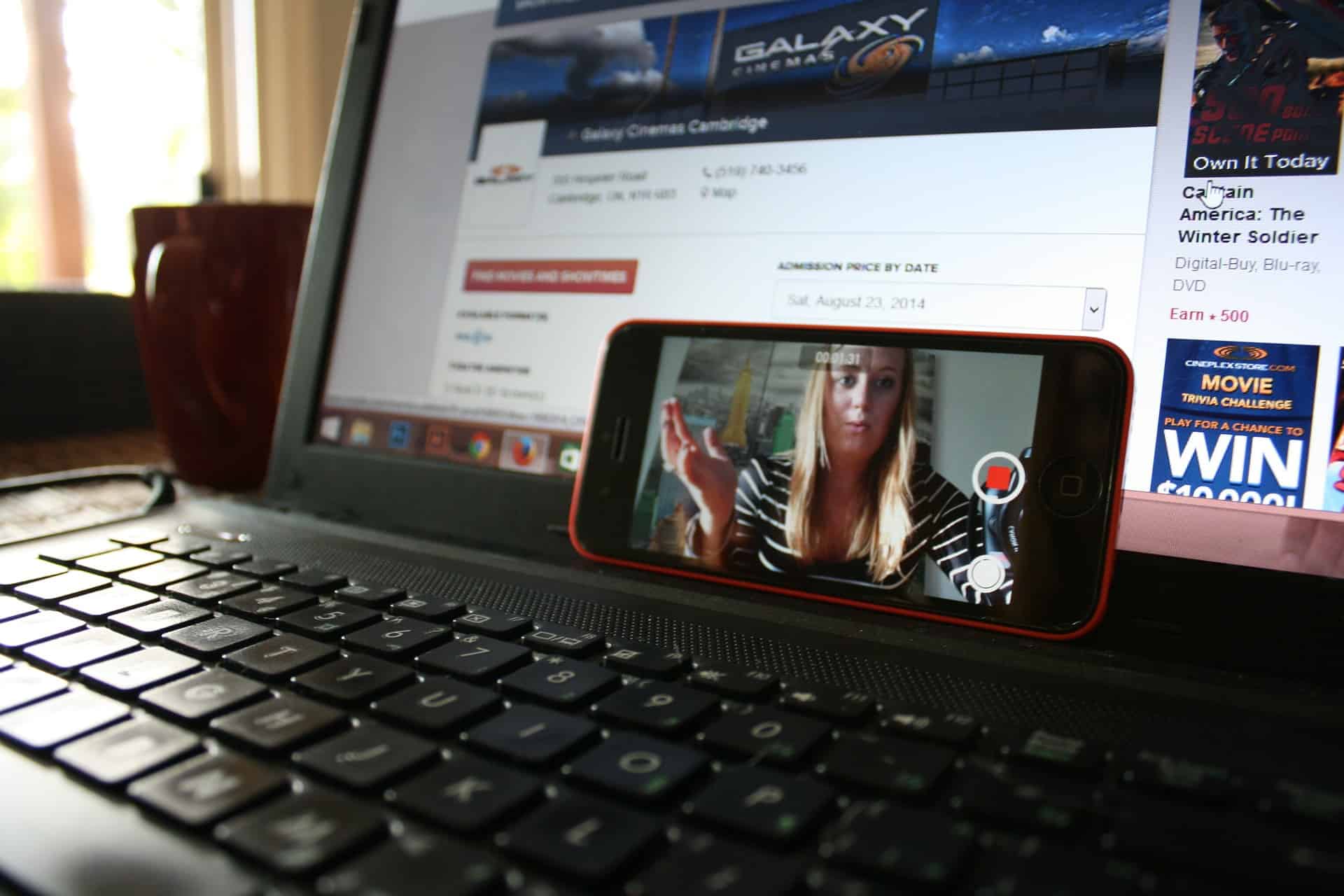 Smartphone propped on a laptop showing a video call, with a cinema website open in the background