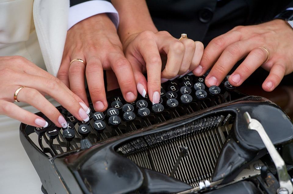 Two pairs of hands typing together on a vintage typewriter keyboard