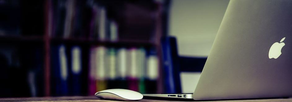 Laptop and wireless mouse on a desk with colourful binder folders in the background