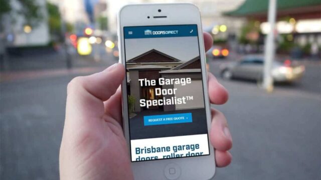 Hand holding a smartphone displaying the Doors Direct mobile website, with a Brisbane street scene in the background