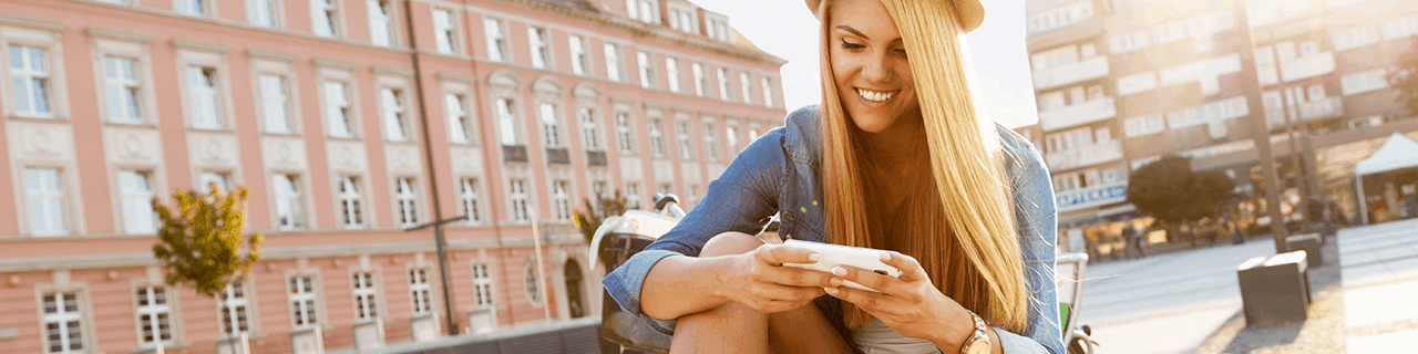 Young woman smiling while using her smartphone outdoors in a European city square on a sunny day