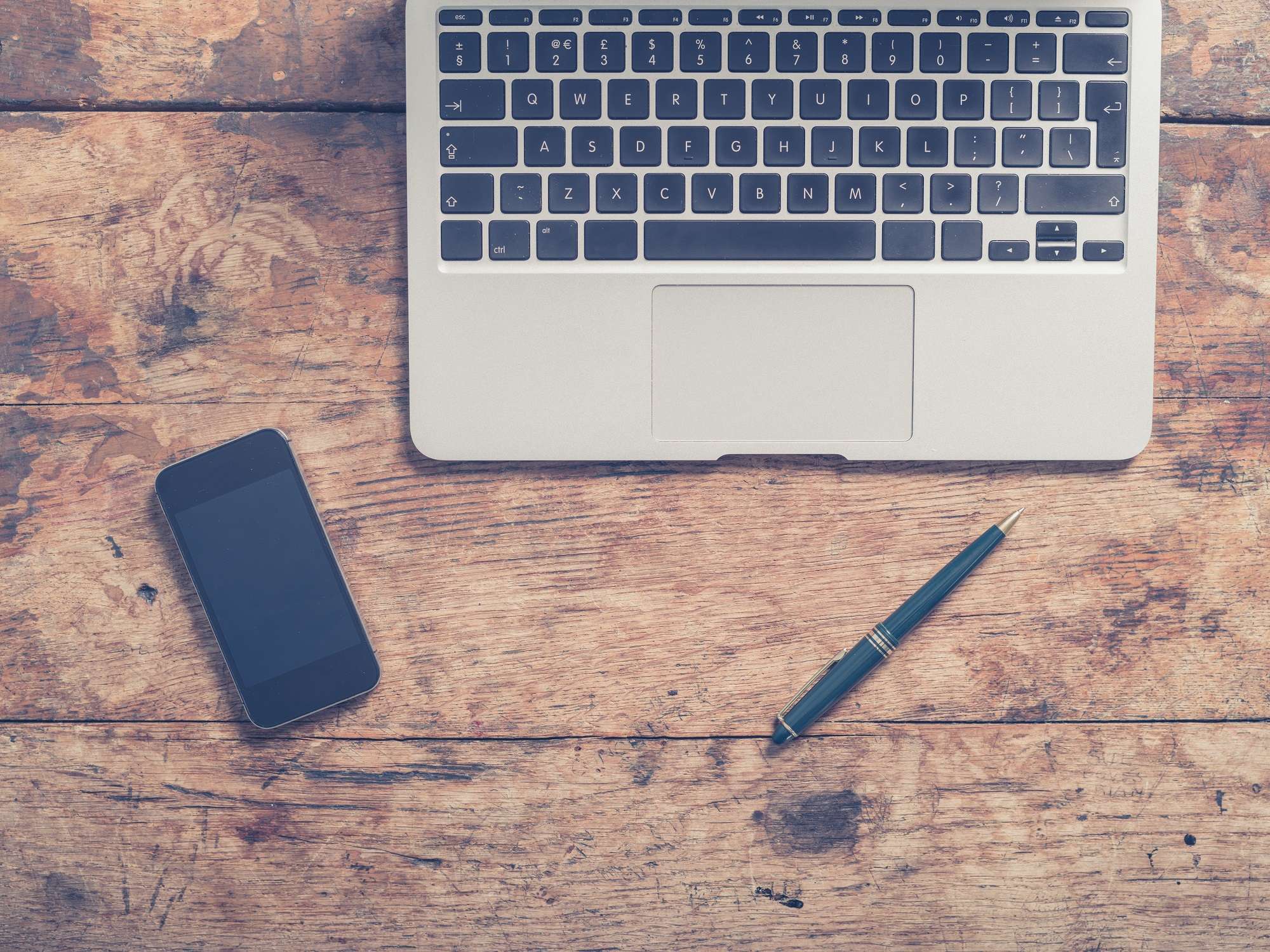 Laptop, smartphone and pen arranged on a wooden desk, used as the featured image for the why you should learn SEO article